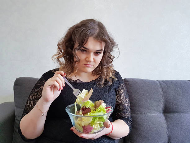 muito linda garota no sofá com uma dieta de salada - overweight women salad frustration - fotografias e filmes do acervo