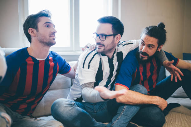 istock Male football supporters hugging and watching game from comfortable sofa 951652368