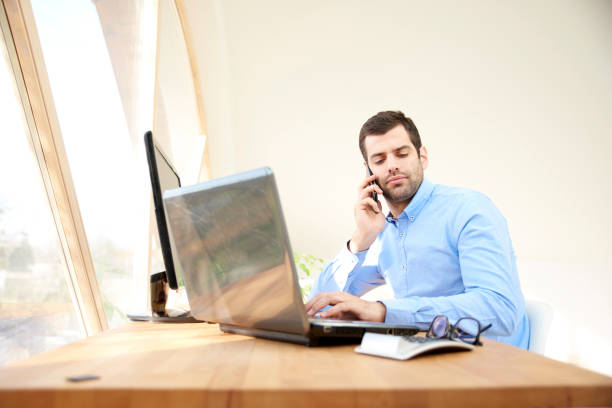 istock Young man consulting with somebody on his mobile phone and using laptop 951668360
