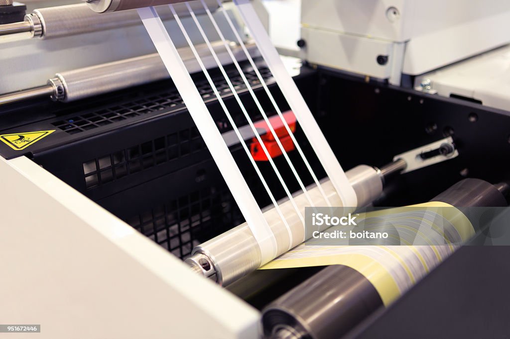 Close-up shot of labels manufacturing on flexo printing machine. Photo detail of matrix waste or trim removal from adhesive material on flexographic press. Label Stock Photo