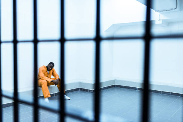 istock african american prisoner sitting on bench behind prison bars 951676410