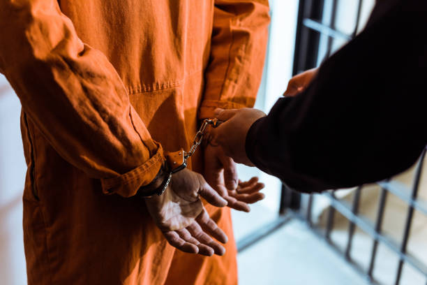 cropped image of prison officer wearing handcuffs on prisoner - cela imagens e fotografias de stock