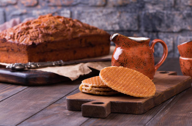 Stack of Stroopwafels or Dutch Waffles with caramel. Traditional Dutch dessert Stroopwafels cake with cups of coffee and milk. Rustic wooden table.