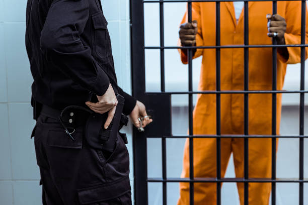 cropped image of prison guard putting hand on gun near prison bars cropped image of prison guard putting hand on gun near prison bars prison guard stock pictures, royalty-free photos & images