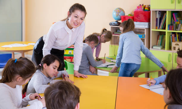 istock Smiling teacher and children sitting at table 951685682