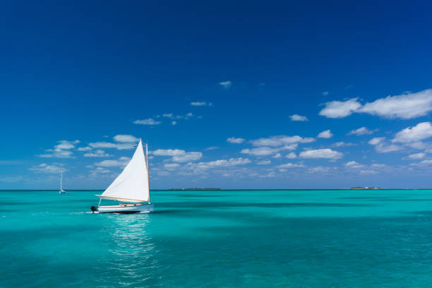 Small sailboat moves through clear and calm waters near Hope Town, Abaco, Bahamas