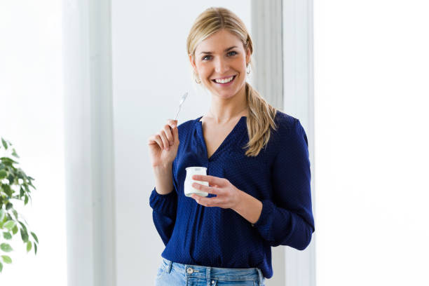 istock Beautiful young woman looking at camera while eating yogurt at home. 951692752