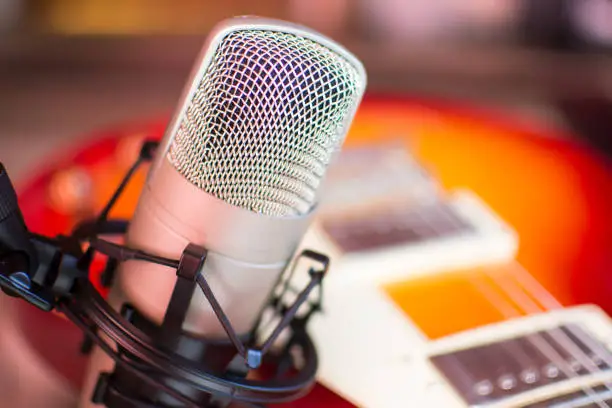 Microphone in home recording studio with red guitar on background