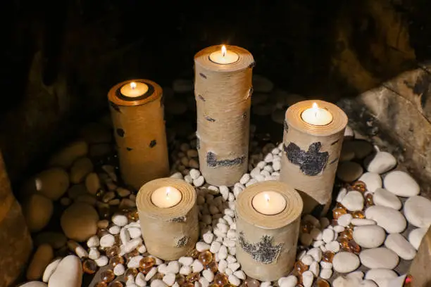 Candleholders that look like birch logs holding replaceable tealight candles and sitting on a bed of decorative stones in a fireplace