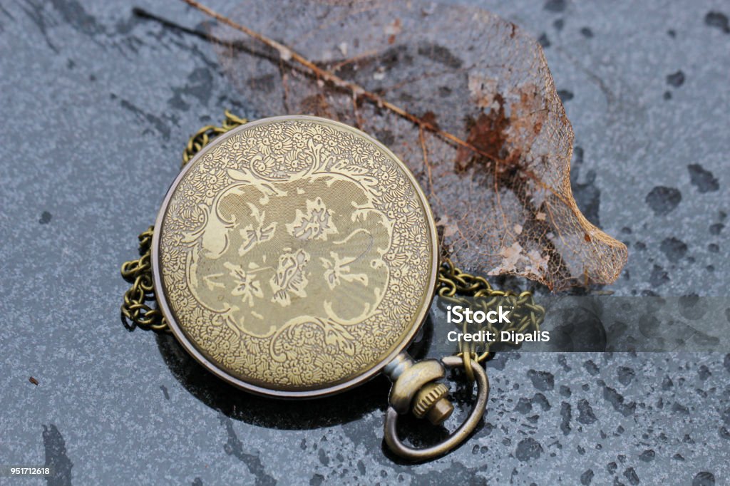 An antique pocket watch A pocket watch on a wet background with an old leaf. Accuracy Stock Photo