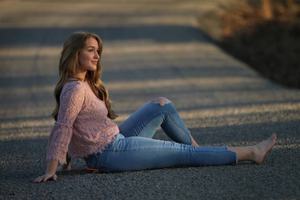 Beautiful Long Hair Blond Teenage Girl setting on a Seldom Traveled Curvy Country Road in the Springtime. Relaxing with bare feet on a tranquil springtime afternoon with the sunshine glistening off the young adult’s long blond hair. traveled stock pictures, royalty-free photos & images