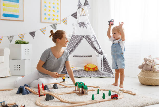 glückliche familie, mutter und kind sohn in spielzeug-eisenbahn im spielzimmer spielen - child playroom parent indoors stock-fotos und bilder