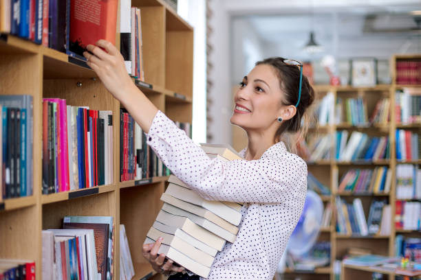 junge frau mit einem stapel bücher in der bibliothek - bibliothekar stock-fotos und bilder