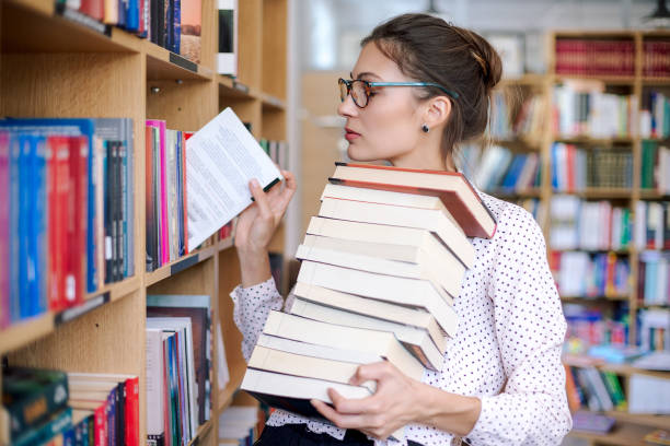 istock Young woman with a stack of books in library 951741224