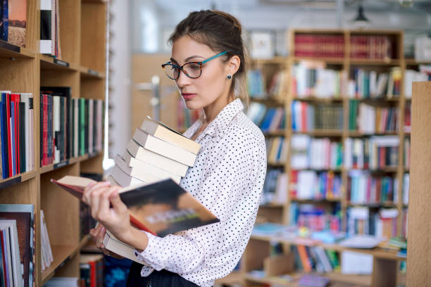 istock Young woman with a stack of books in library 951741276