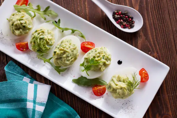 Deviled eggs with avocado puree and spices decorated with herbs and cherry tomatoes