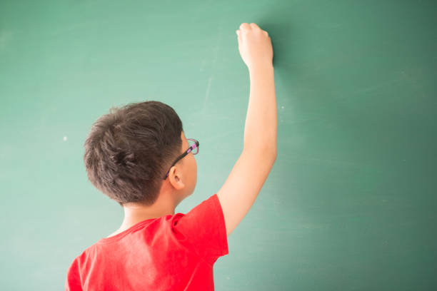 istock Little asian boy writing on empty green board at school 951820592
