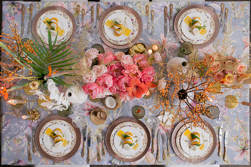 Festive table decor. Many pastel colors. Luxury wedding, party, birthday. Copper chairs and dishes, gold, silver cutlery.  Chinese, European, chinoiserie style. candle, mozzarella, persimmons. Above.