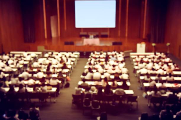 blurred image of students, audience and keynote speaker for freshman orientation day or lecture in international conference hall during graduation ceremony. event university. vintage film color. - winners podium audio imagens e fotografias de stock