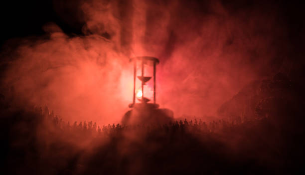 Silhouette of a large crowd of people in forest at night standing against a big hourglass with toned light beams on foggy background. Time concept. Silhouette of a large crowd of people in forest at night standing against a big hourglass with toned light beams on foggy background. Time concept. Hourglass measuring the passing time cologne germany stock pictures, royalty-free photos & images