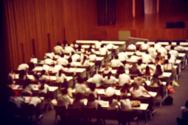 Blurred image of students, audience and keynote speaker for freshman orientation day or lecture in international conference hall during graduation ceremony. event university. vintage film color.