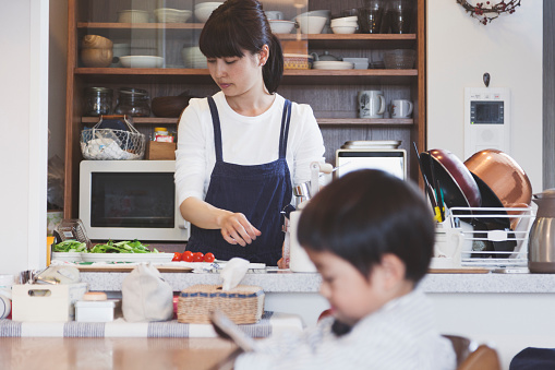 Japanese mother cooking in the kitchen and her son waiting for meal with using a digital tablet.