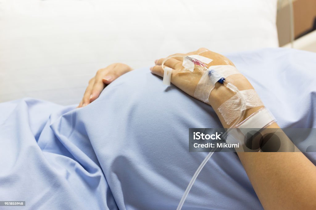 Asian Pregnant Woman patient is on drip receiving a saline solution on bed VIP room at hospital. Asian Pregnant Woman patient is on drip receiving a saline solution on bed VIP room at hospital, selective focus. Pregnant Stock Photo