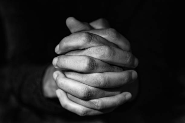 man with his hands clasped, in black and white closeup of the hands of a young caucasian man with his hands clasped, in black and white hands clasped stock pictures, royalty-free photos & images