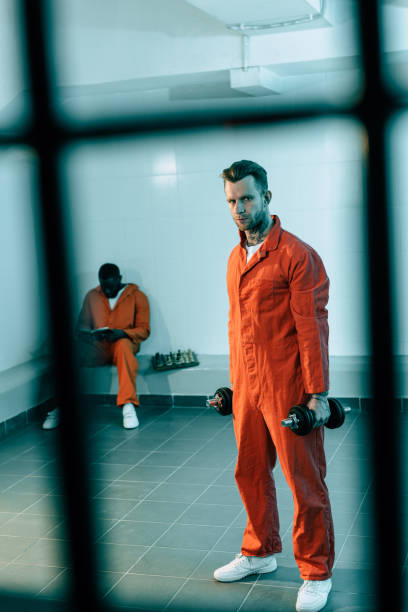 prisoner training with dumbbells in prison room and looking at camera