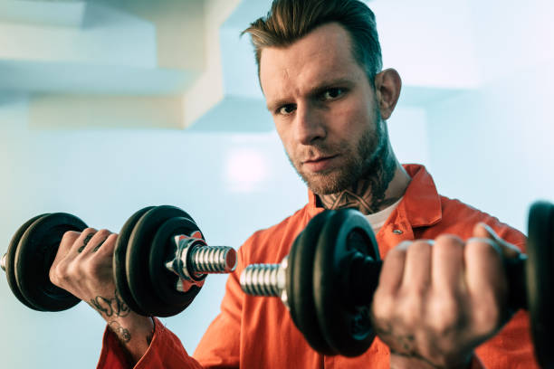 tattooed prisoner training with dumbbells in prison room