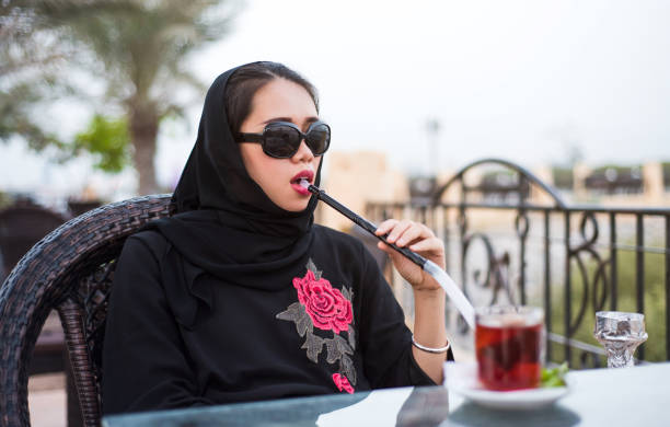 Muslim woman smoking shisha outdoors Muslim woman smoking shisha in a bar outdoors smoking women luxury cigar stock pictures, royalty-free photos & images