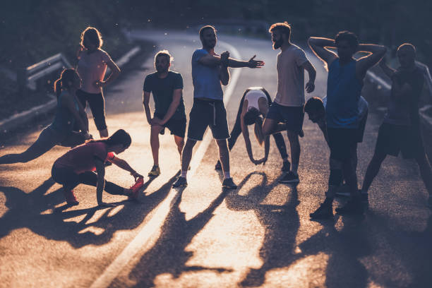 Large group of marathon runners warming up on a road at sunset. Marathon runners stretching while warming up before the race at sunset. off track running stock pictures, royalty-free photos & images