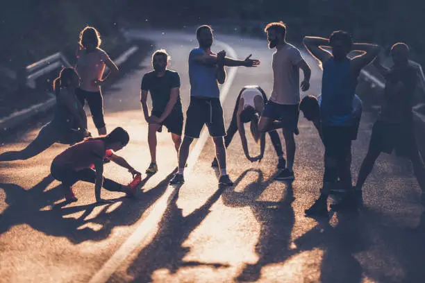 Photo of Large group of marathon runners warming up on a road at sunset.