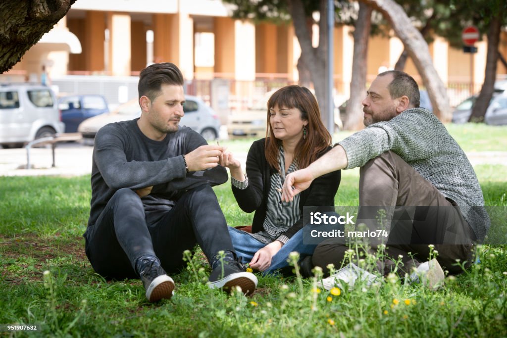 três amigos sentado na grama no parque público, fumar - Foto de stock de Maconha royalty-free