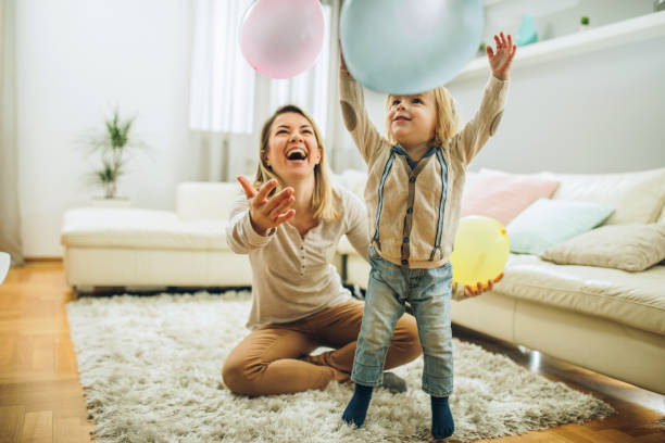 Playful mother and son having fun with balloons in the living room. Happy mother and her small son playing with a balloons at home. Focus is on boy. nanny photos stock pictures, royalty-free photos & images