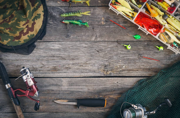 equipamento de pesca - pesca fiação, faca de caça, anzóis e iscas, uma rede de pesca e macacões. sobre um fundo de madeira, vista superior. espaço de cópia - fishing hook catch of fish fishing fishing tackle - fotografias e filmes do acervo