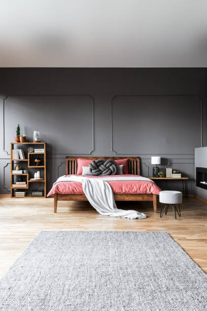 istock A pink bedding on a king-size bed standing in a spacious room interior in front of a grey rug and between a shelf and a bedside table 951914440