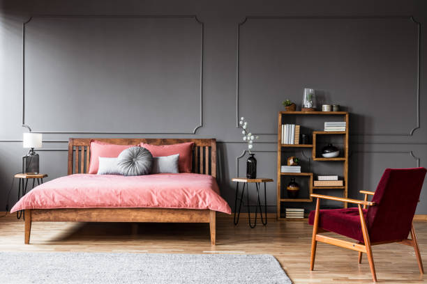 istock A king-size bed standing in a dark, spacious room between the bedside table with a wooden shelf next to one of them and a red armchair in front of them 951914444