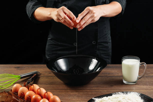 male hands chef chefs break the egg on a wooden brown table in a black bowl. black background. the concept of cooking food. close-up. - cake making mixing eggs imagens e fotografias de stock