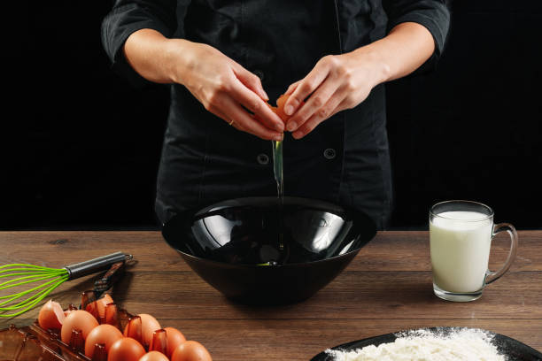 male hands chef chefs break the egg on a wooden brown table in a black bowl. black background. the concept of cooking food. close-up. - cake making mixing eggs imagens e fotografias de stock