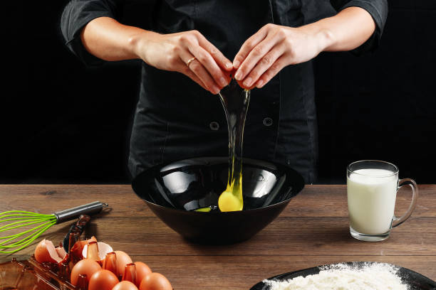 male hands chef chefs break the egg on a wooden brown table in a black bowl. black background. the concept of cooking food. close-up. - cake making mixing eggs imagens e fotografias de stock