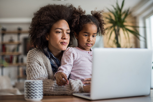 African American mother and daughter surfing the Internet on laptop at home.