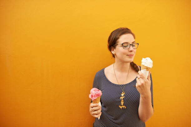 Who says you need to have a favorite flavor? Shot of an attractive young woman eating two ice creams against an orange background hedgehog mushroom stock pictures, royalty-free photos & images
