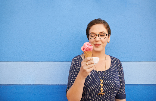 Shot of an attractive young woman eating an ice cream against a blue background