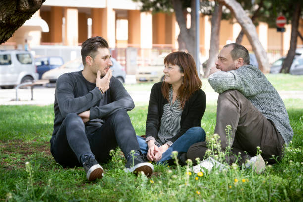 istock three friends sitting on the grass in the public park, smoking 951928044