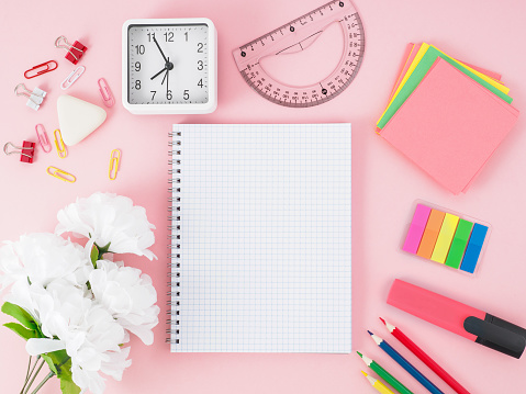 Top view of modern bright pink office desktop with notebook in a cage, flowers, school supplies on table, empty space for text. Back to school concept.