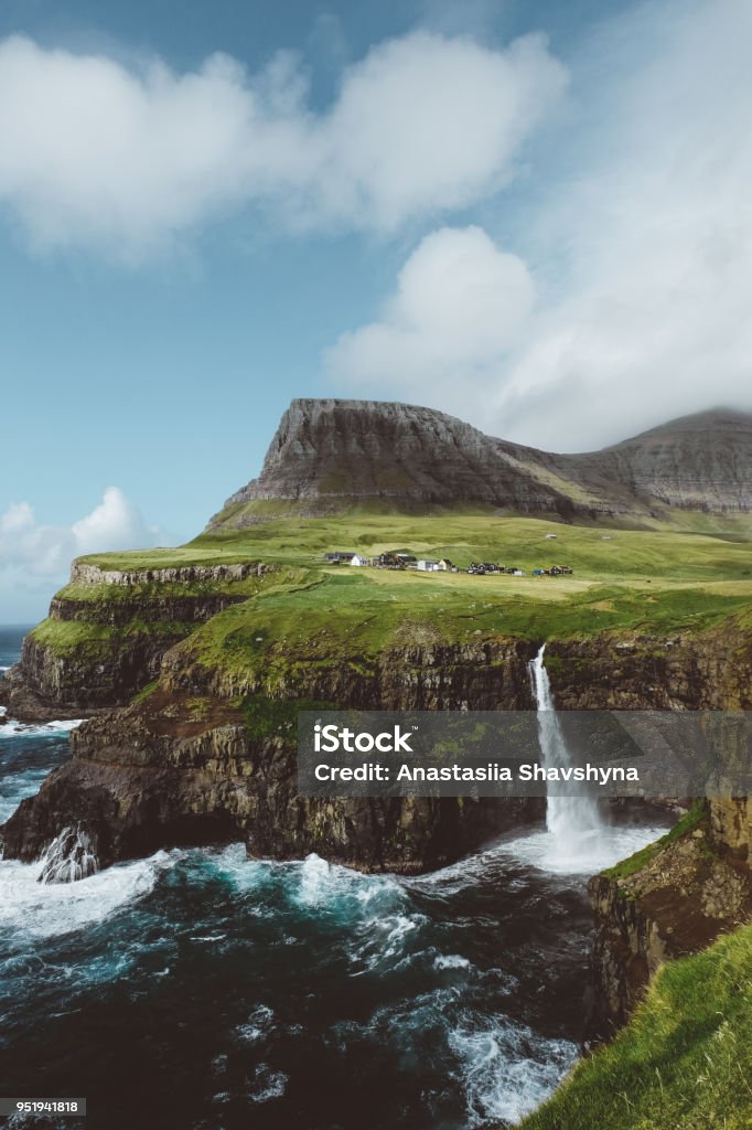 Small village above one of themes beautiful waterfalls in the world on Faroe Islands Dramatic view of Gasadalur waterfall falling into the ocean on Faroe Islands Faroe Islands Stock Photo