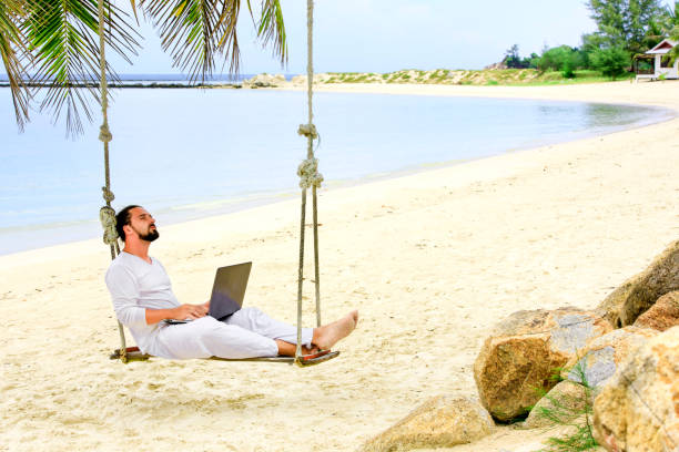 mann, der arbeitet mit einem laptop auf einer hängematte am strand. show-sieg - beach men isolated tourist stock-fotos und bilder