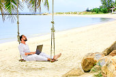 Man working with a laptop, on a hammock in the beach. Show win