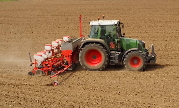 istock Tractor with a modern sowing seeds machine in a newly plowed field in springtime. Side view. Plowed land on background 951968624